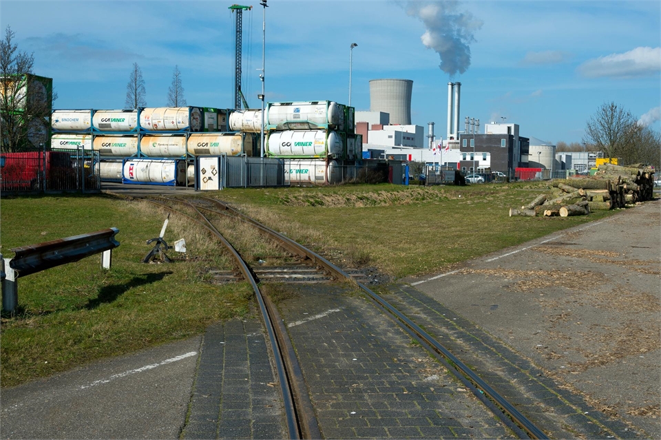 Noord-Brabant - Havengebied Moerdijk: foto van spoorlijn die door een weg heen loopt met in de verte opslagtanks.